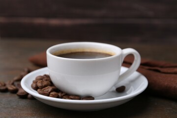 Fototapeta premium Aromatic coffee in cup, beans and saucer on wooden table, closeup
