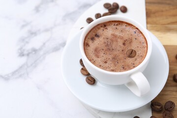 Aromatic coffee in cup, beans and saucer on white marble table, closeup. Space for text