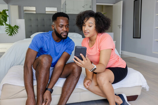 Couple sitting on bed, sharing smartphone, enjoying relaxed time together at home