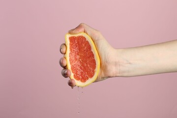 Woman squeezing grapefruit on pink background, closeup