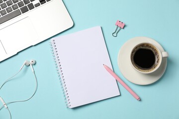 Fototapeta premium Notebook, pen, earphones, coffee, binder clip and laptop on light blue background, flat lay