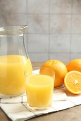 Fresh orange juice and fruits on wooden table against grey tiled wall, closeup
