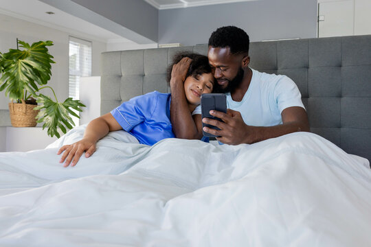 Couple relaxing in bed, smiling while looking at smartphone together at home
