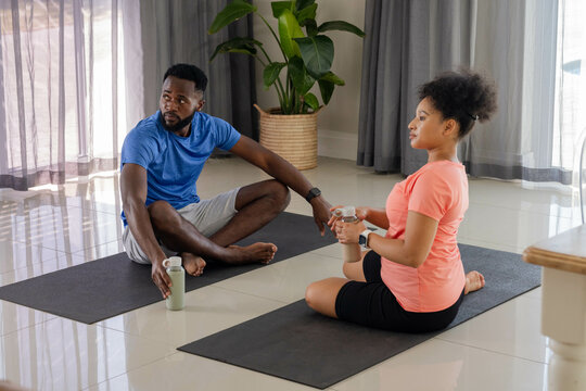 Couple relaxing on yoga mats at home, holding water bottles, enjoying conversation