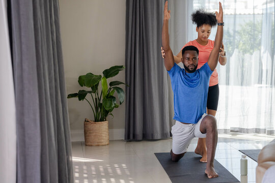 Couple practicing yoga at home, man stretching with partner's guidance