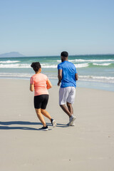 Fototapeta premium African American couple jogging on beach, enjoying sunny day by ocean