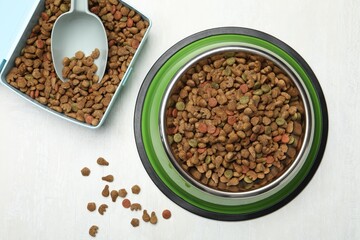 Dry pet food in feeding bowl, container and scoop on light background, flat lay