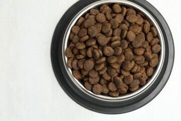 Dry pet food in feeding bowl on light background, top view
