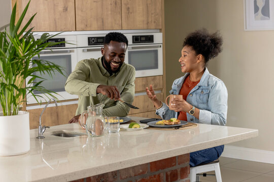 Couple enjoying breakfast together at modern kitchen counter, sharing laughter