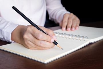 closeup view of woman hand using pencil writing on blank white page notebook while sitting at the table.