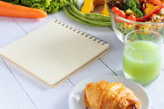 blank notebook planner with salad, fruit juice, bread and vegetable on dining table. calories control, meal plan, food diet and weight loss concept.