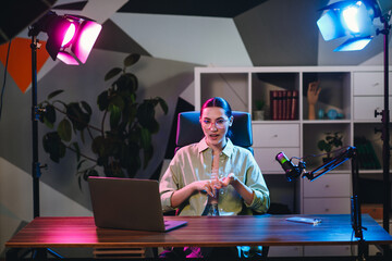 Young businesswoman in casual attire presenting content in a modern home office studio with...