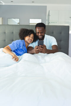 Couple relaxing in bed, smiling while watching smartphone together at home