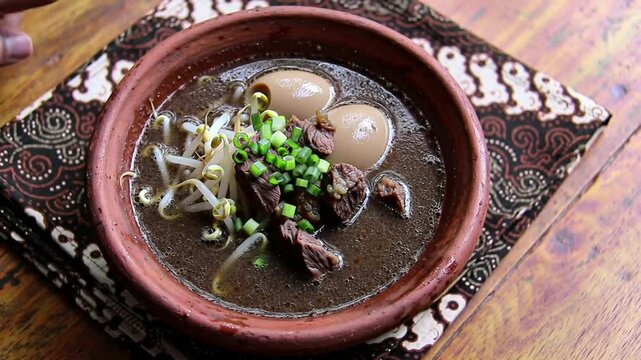 Traditional Indonesian Rawon Beef Soup in Rustic Clay Bowl with Garnishes