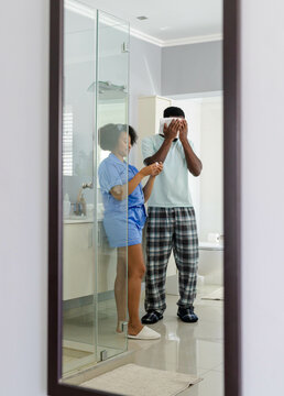African American couple in pajamas brushing teeth together in bathroom mirror
