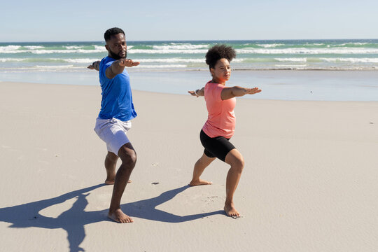 Couple practicing yoga on beach, focusing on balance and strength together