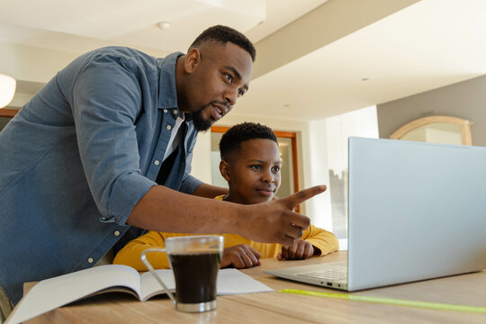 Father guiding son on laptop at home, focusing on learning together
