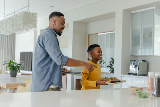 African American father and son preparing breakfast together in modern kitchen, smiling and bonding