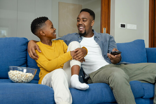 African American father and son enjoying movie time on couch with popcorn and remote