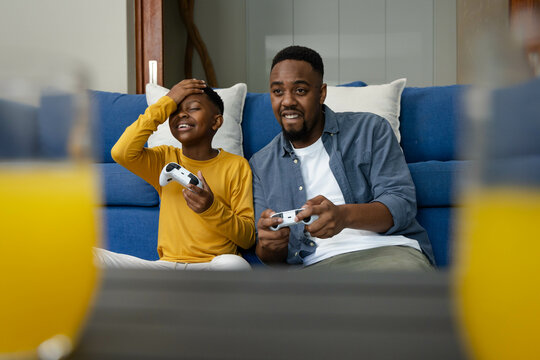 African American father and son playing video games on couch, enjoying quality time together