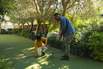 African American father teaching son to play golf on backyard putting green