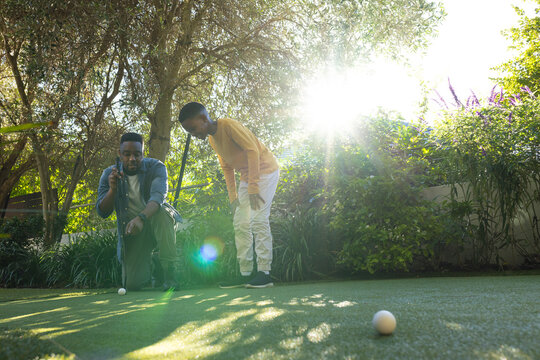 Father and son playing mini-golf on sunny day, enjoying outdoor activity together