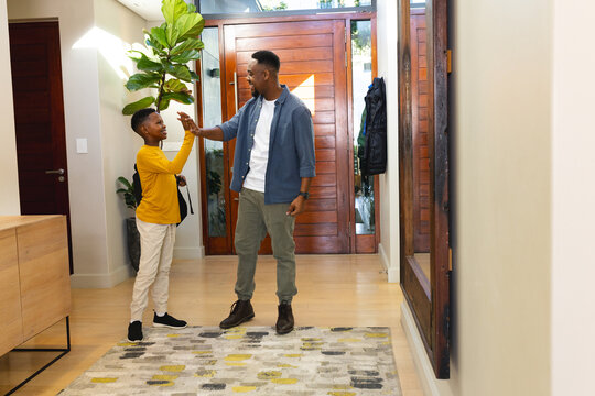 African American father and son high-fiving in modern home entryway, feeling excited