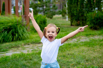Happy baby girl on the green lawn in the summer, children's holidays, little girl laughing and having fun in the summer in the park and shouting hooray