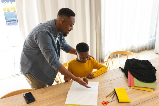 Father helping son with homework at home, pointing at notebook, smiling together