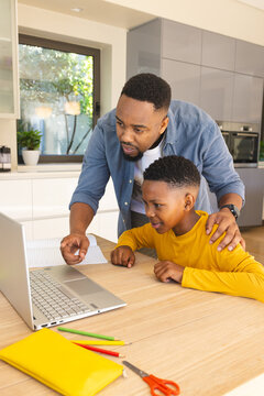 African American father helping son with homework on laptop at kitchen table