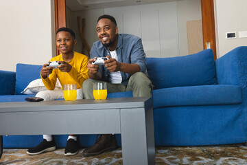 African American father and son playing video games on couch, enjoying quality time