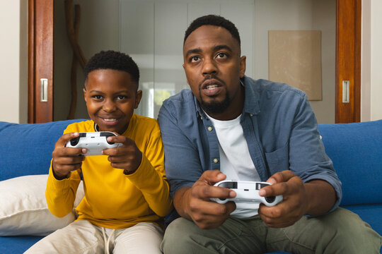 African American father and son playing video games on couch, enjoying time together