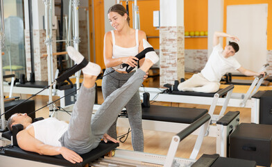Man athlete performs exercises to increase leg strength using sling reformer. Girl trainer mentors...