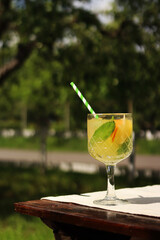 Drink on a garden table on a hot summer day. Glass with cocktail on a wooden table outdoors. Lemonade on a table against the background of blurred nature. Lemonade or other drink in a glass goblet