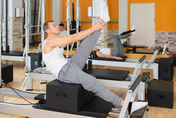 Man athlete works out in gym and performs set of exercises to stretch leg muscles with help of...