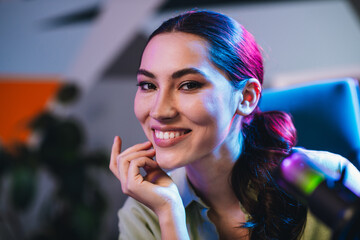 Young professional woman in a casual setting with vibrant colored lights, sitting near a microphone