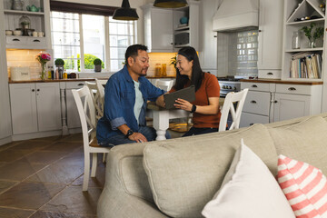 Mature Asian couple in kitchen using tablet, smiling and enjoying time together