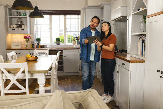 Asian couple in kitchen using tablet, planning home renovation together