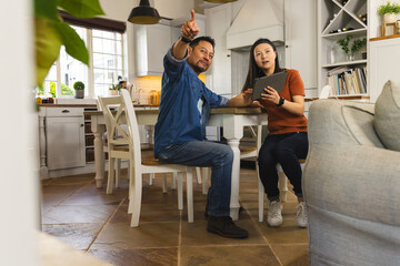 Asian couple in kitchen discussing home renovation plans using digital tablet