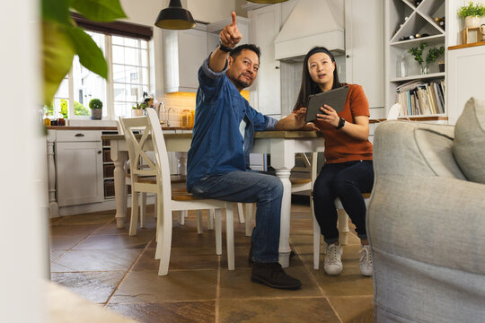 Asian couple in kitchen discussing home renovation plans using digital tablet