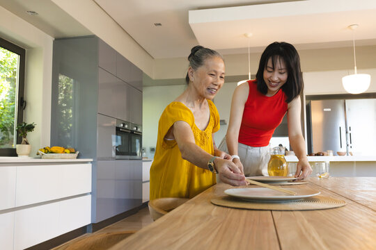 Asian senior mother and daughter setting dining table together, smiling and enjoying time