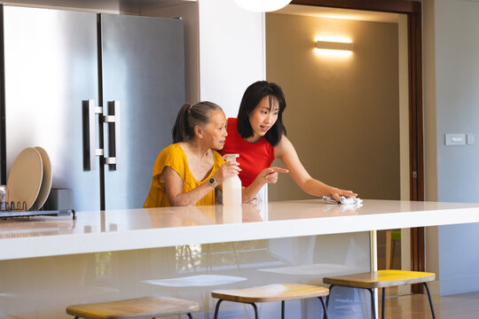 Asian senior mother and daughter cleaning kitchen counter together, enjoying quality time