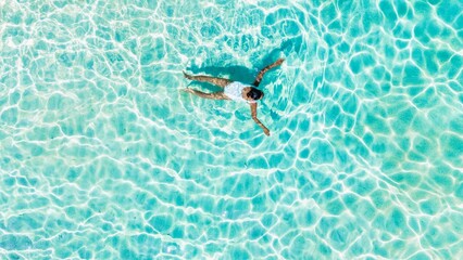 A woman enjoys a moment of relaxation while floating in the warm, crystal-clear waters of Koh Munnork Island in Rayong, Thailand. The vibrant colors reflect the peaceful surroundings.