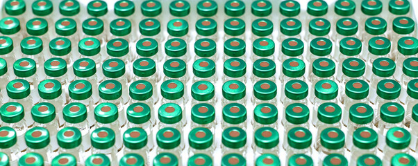 Ampoules with green caps neatly arranged in a safety box on a sterile lab surface. Concept...