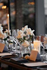 Elegant table setting for a sophisticated celebration on a luxurious black table. Golden candleholders, wine glasses, white rose, napkins, and a paper name card create a refined atmosphere.