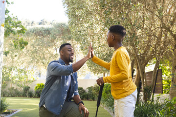 African American father and son playing mini golf in backyard garden, with club in hand
