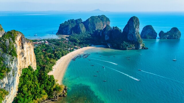 Railay Beach in Krabi Thailand showcases breathtaking limestone cliffs and vibrant waters under a clear sky. Visitors can enjoy boating alongside lush tropical greenery, creating a paradise.