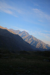 Mountain range illuminated by the soft glow of evening light, with dramatic shadows and a clear sky above. Perfect for themes of adventure, travel, solitude, and natural landscapes.