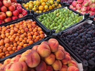 fruits displayed in crates at a farmers market. Includes peaches, apricots, figs, apples, green and yellow varieties, arranged in an eye-catching pattern.

