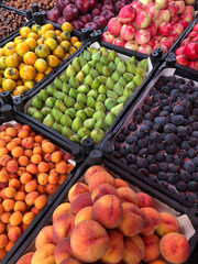 display of assorted fresh fruits at a farmers market. Crates filled with peaches, apricots, figs, apples, persimmons, and chestnuts arranged in neat, colorful rows. Natural and healthy food.